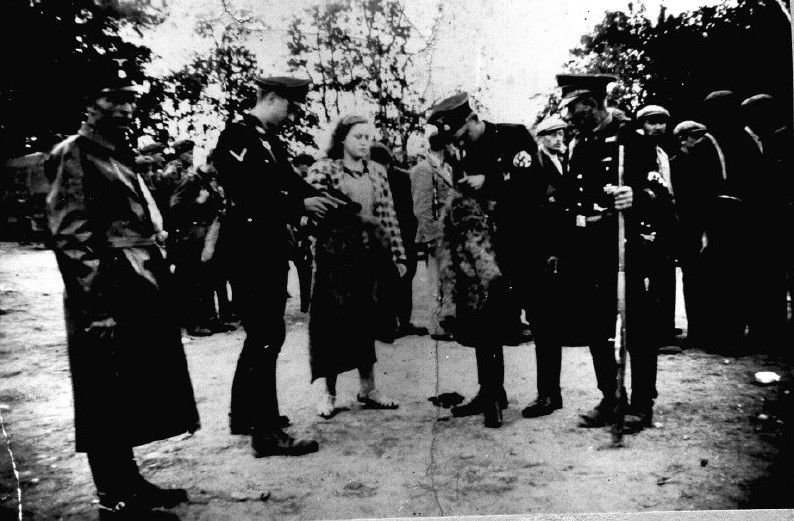 Armed German SS men in a Lithuanian city, inspecting the clothes of a Jewish woman.